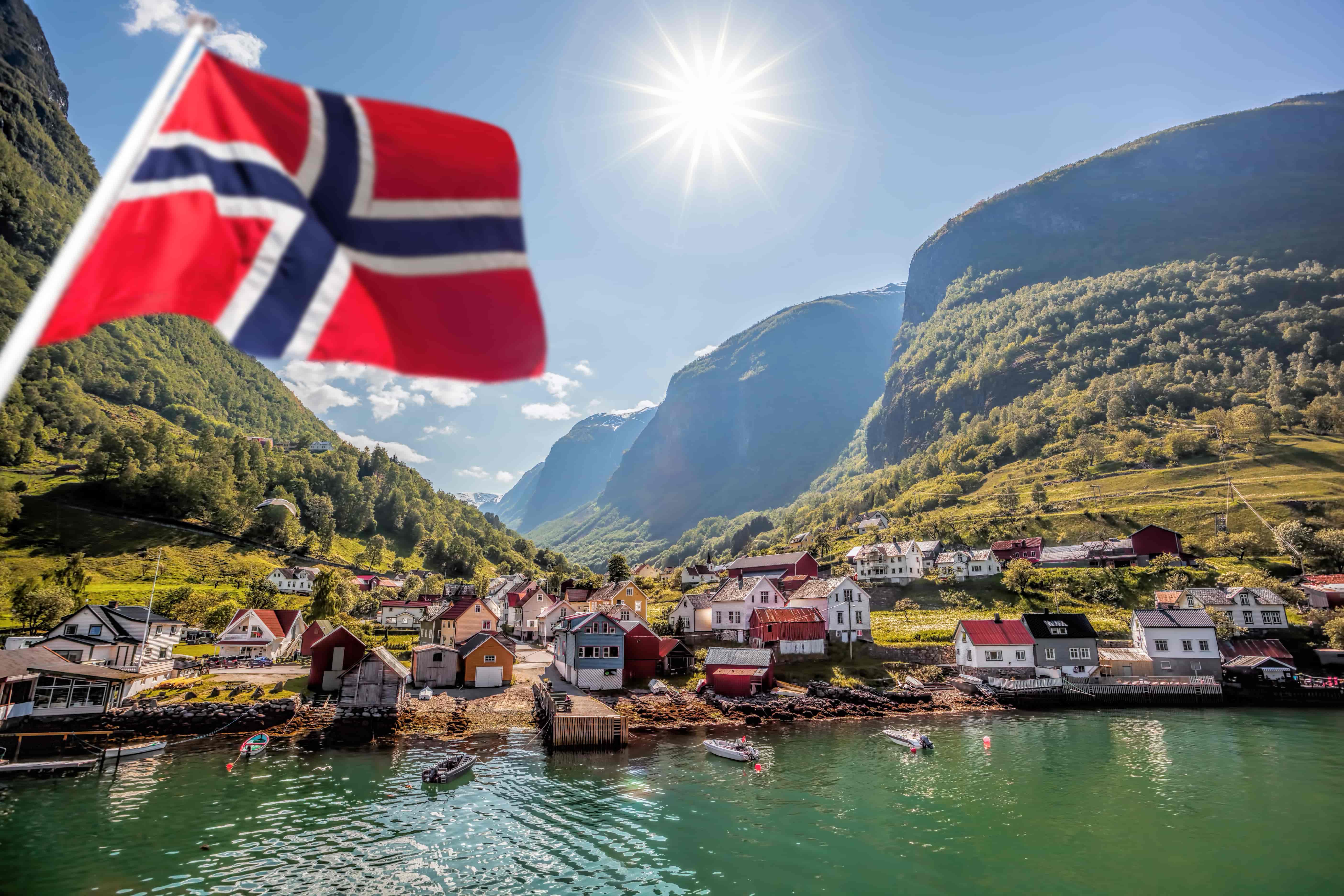 Im Vordergrund ist eine Flagge von Norwegen zu sehen und im Hintergrund ein kleines Küstendorf.