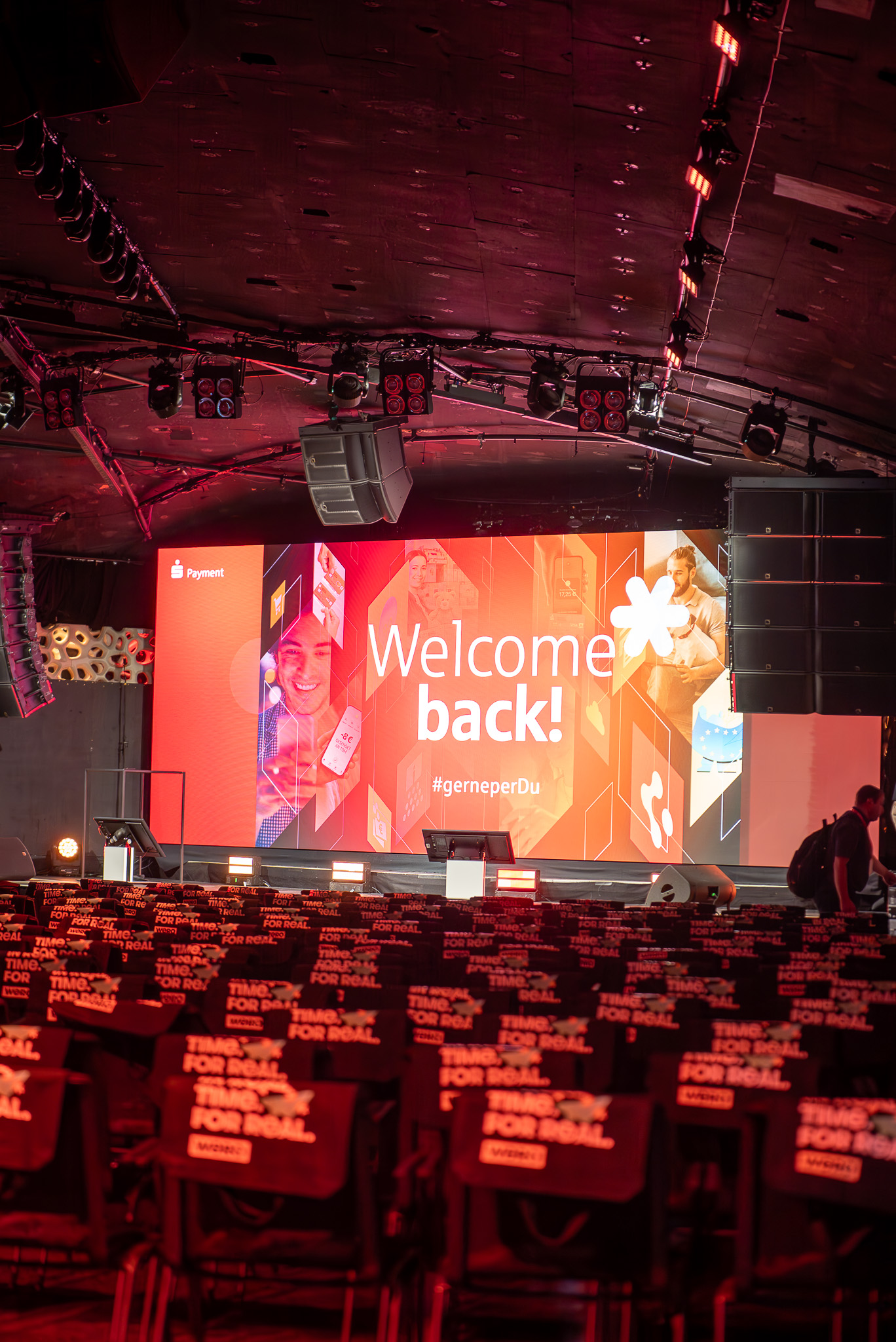 Eine Bühne mit einem LED-Bildschirm vom S-Payment-Sysmposium. Die Stühle und Veranstaltungshalle sind jedoch leer.