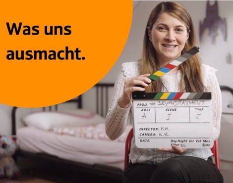 Karriere-Website junge Frau sitzt auf einem Stuhl in einem Zimmer mit Filmklappe in der Hand; schwarz-weiß Bild mit orangenem Gestaltungselement rechts