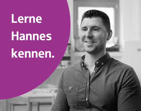 schwarz-weiß Bild: Mitarbeiter Hannes Neumann sitzt auf einem Stuhl und lächelt. Links ein rundes lila Gestaltungselement.