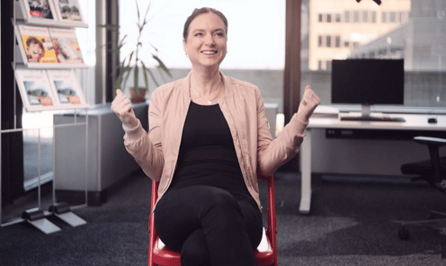 Mitarbeiterin Tanja Weiss sitzt auf einem roten Stuhl mitten im Büro und jubelt