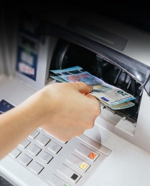 Nahaufnahme einer Hand, die Bargeld und Euro-Scheine aus dem Bankautomaten abhebt.
