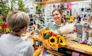 Verkäuferin in einem Blumenladen kassiert Kundin mit der Sparkassenkarte ab und übergibt einen Blumenstrauß