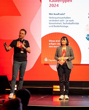 Michael Ullmann und Tanja Moll halten einen Vortrag und stehen dabei auf der Bühne. Michael und Tanja arbeiten bei der S-Payment